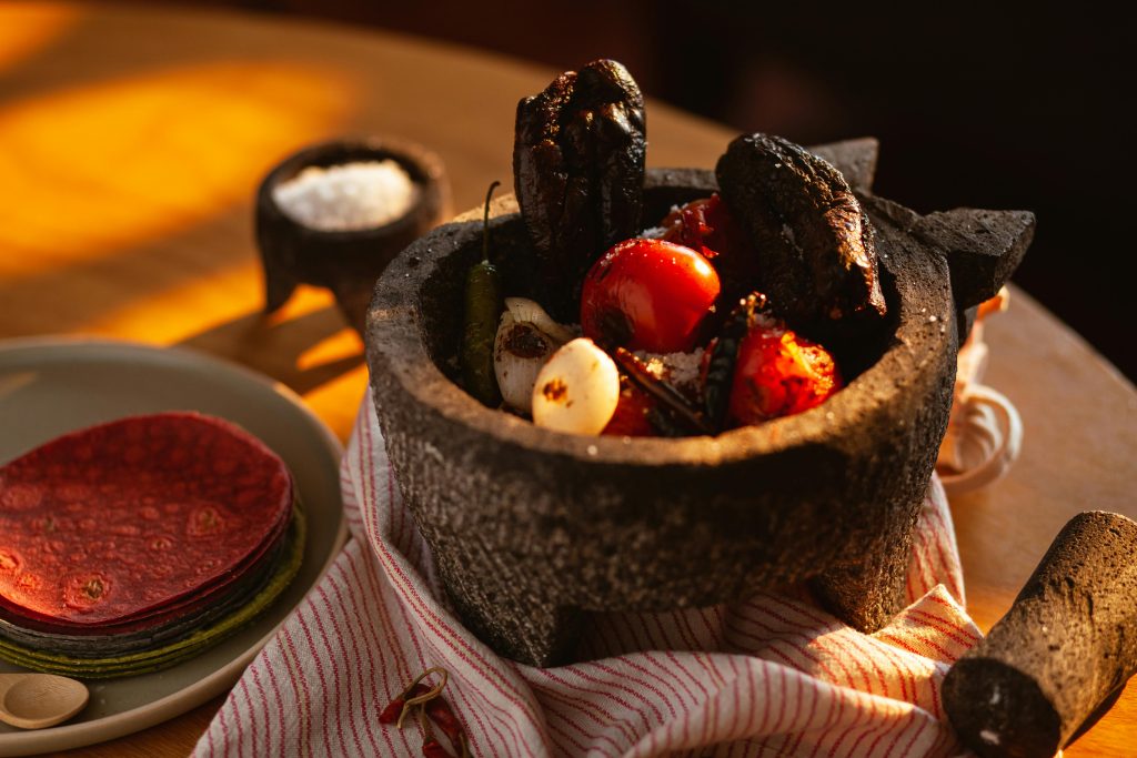 A variety of traditional Mexican ingredients in a rustic stone mortar with warm lighting.